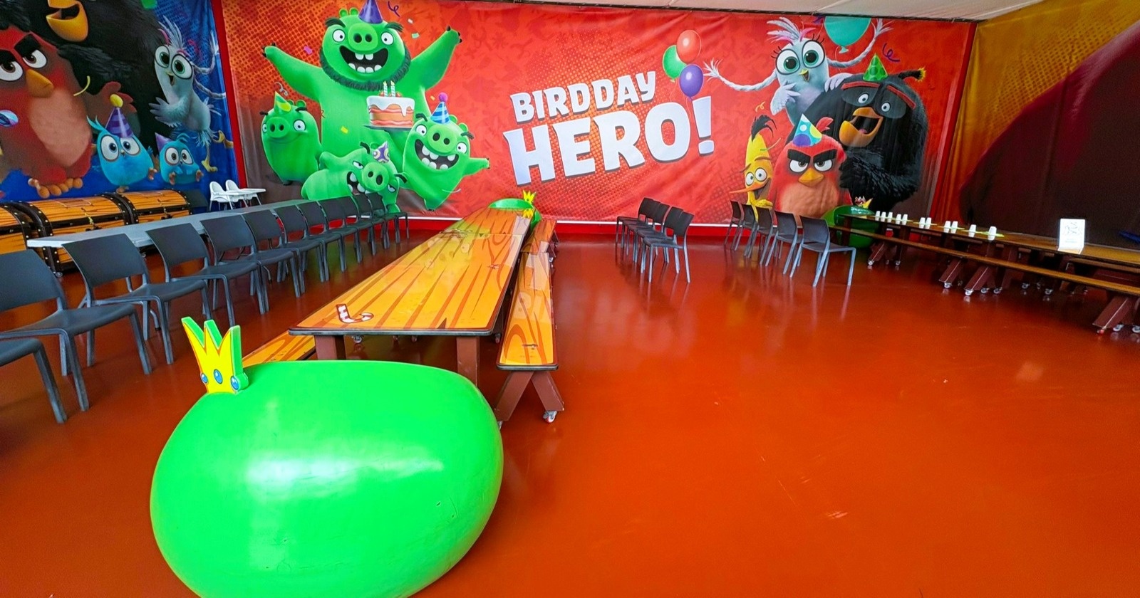 Party room decorated with cartoon bird and pig characters, empty tables and chairs.