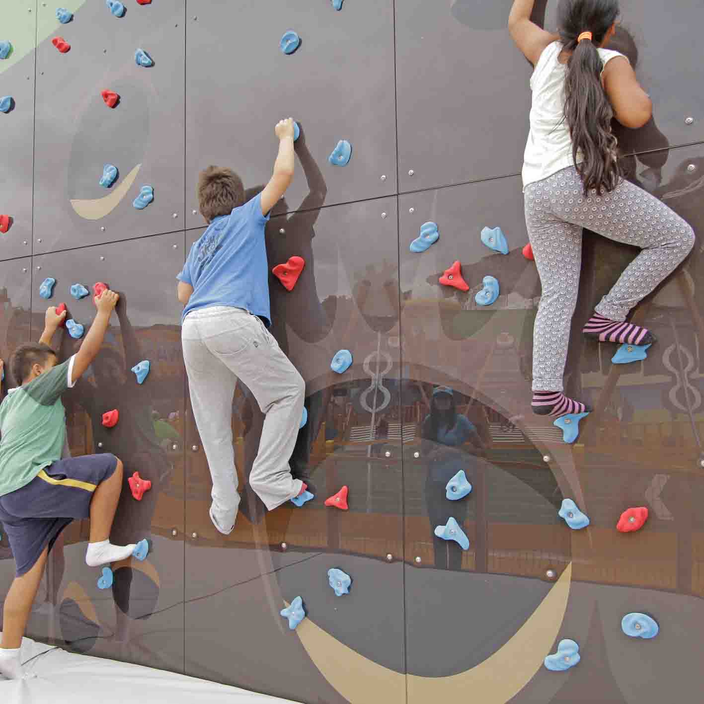 Three children climbing a wall with red and blue holds.