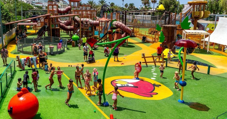 Children playing at a colorful outdoor water park with slides and water features.