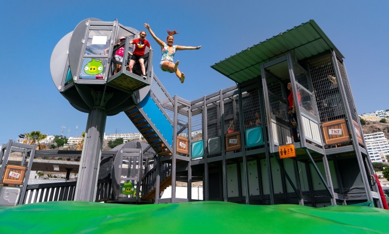 Two people jumping from a themed play structure with slides and nets.
