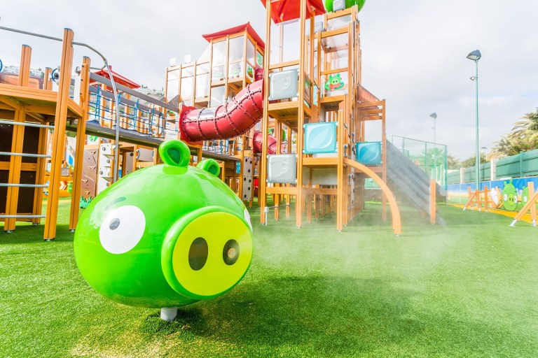 Colorful playground with slide and green pig character on grass.
