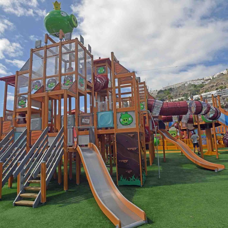 Large outdoor playground with slides and climbing structures under a blue sky.