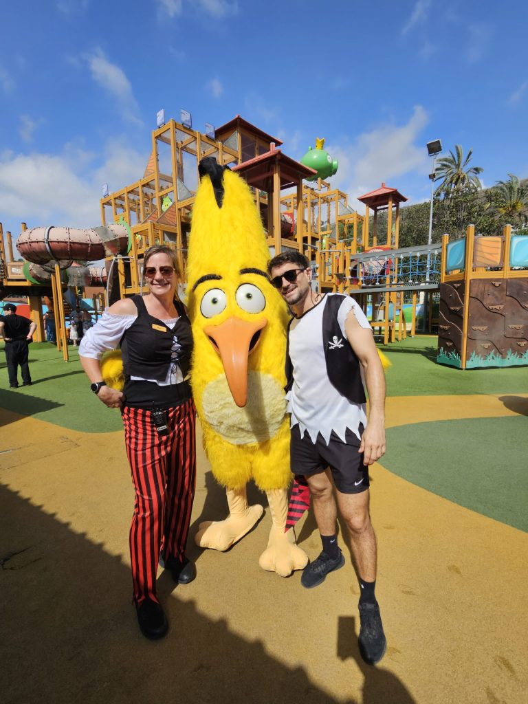 Two people in costumes with a tall yellow bird character in a theme park.