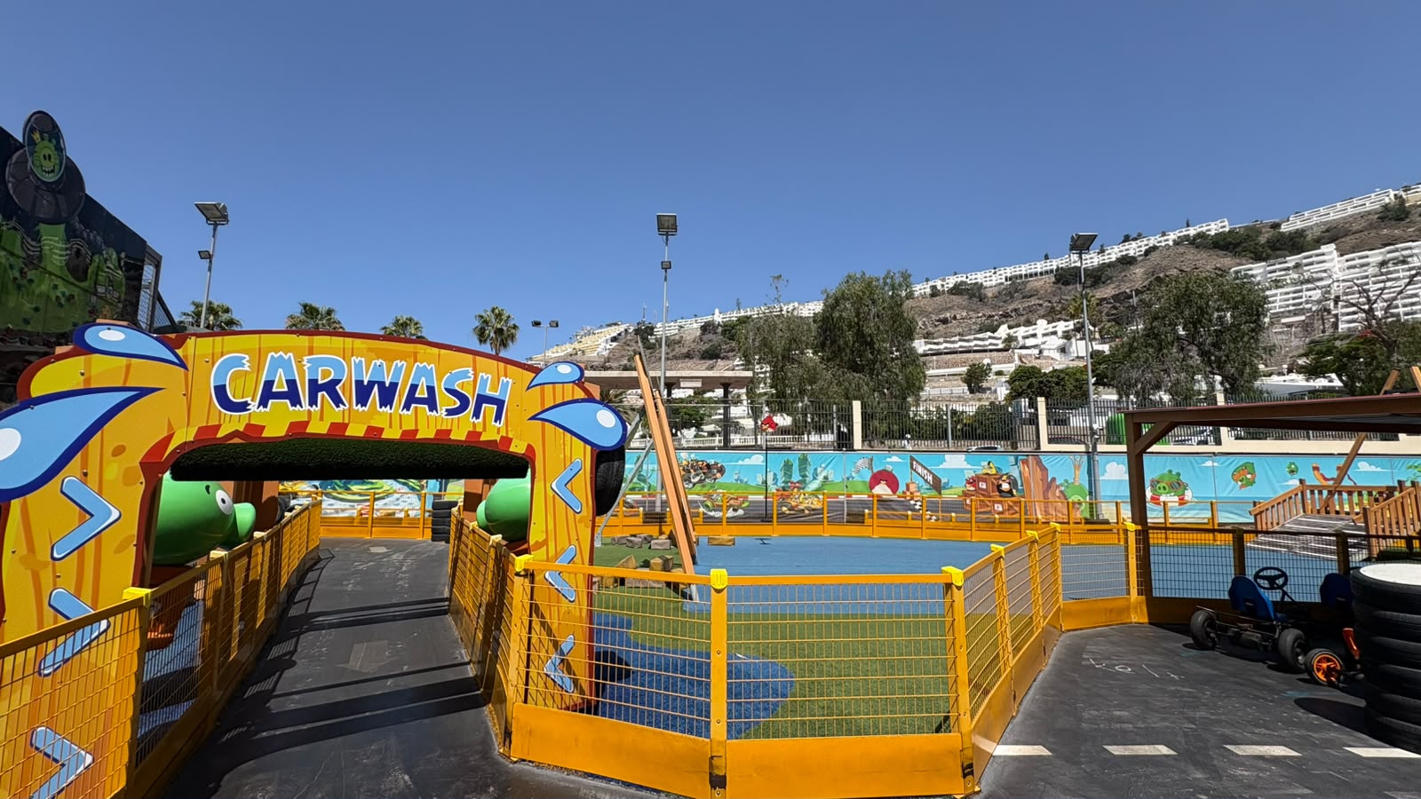 Colorful children's carwash-themed play area with slides and fences under a clear sky.