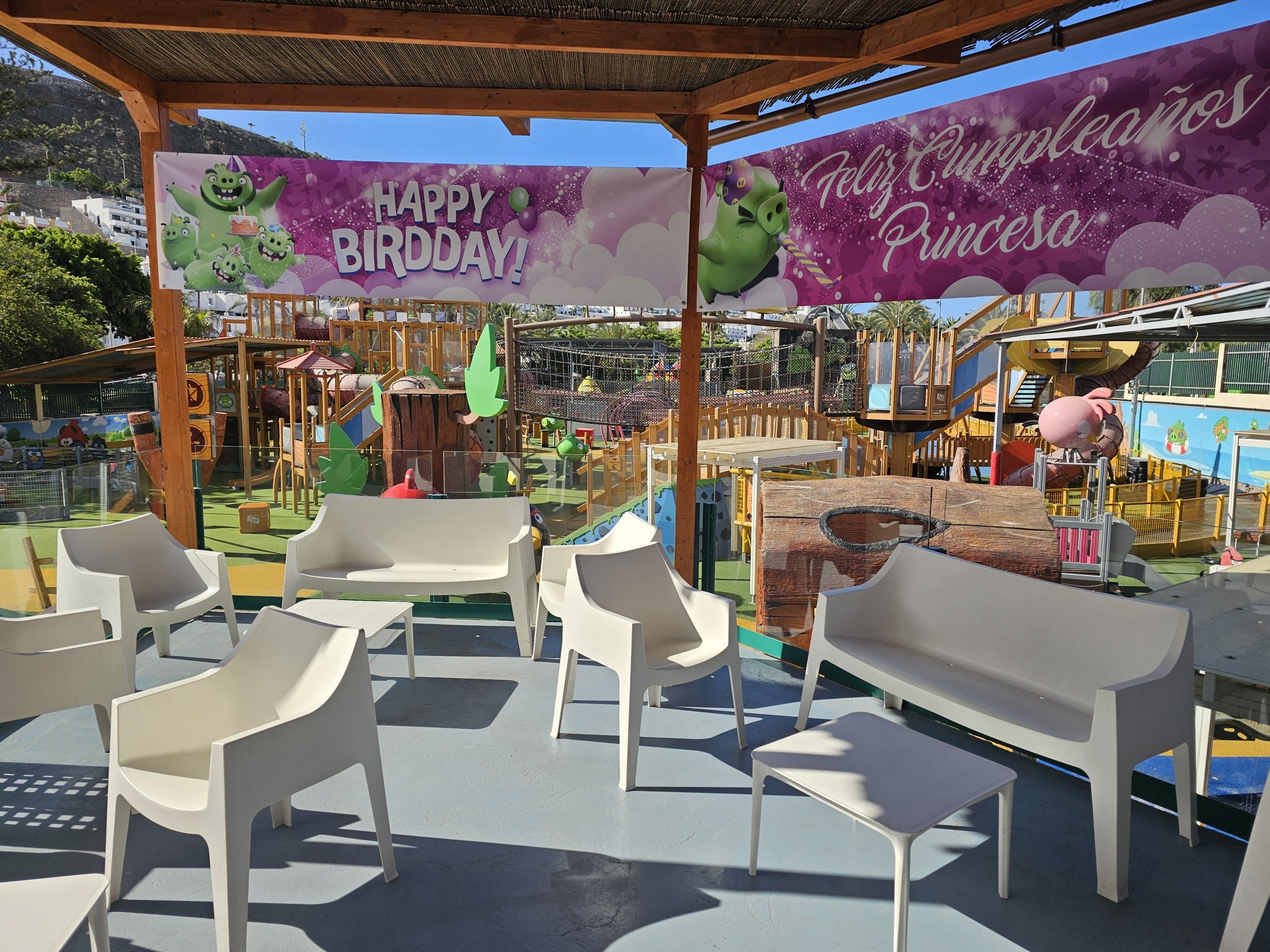Empty chairs on a patio with a playground banner above, reading 'Happy Birthday' and 'Feliz Cumpleaños Princesa'.