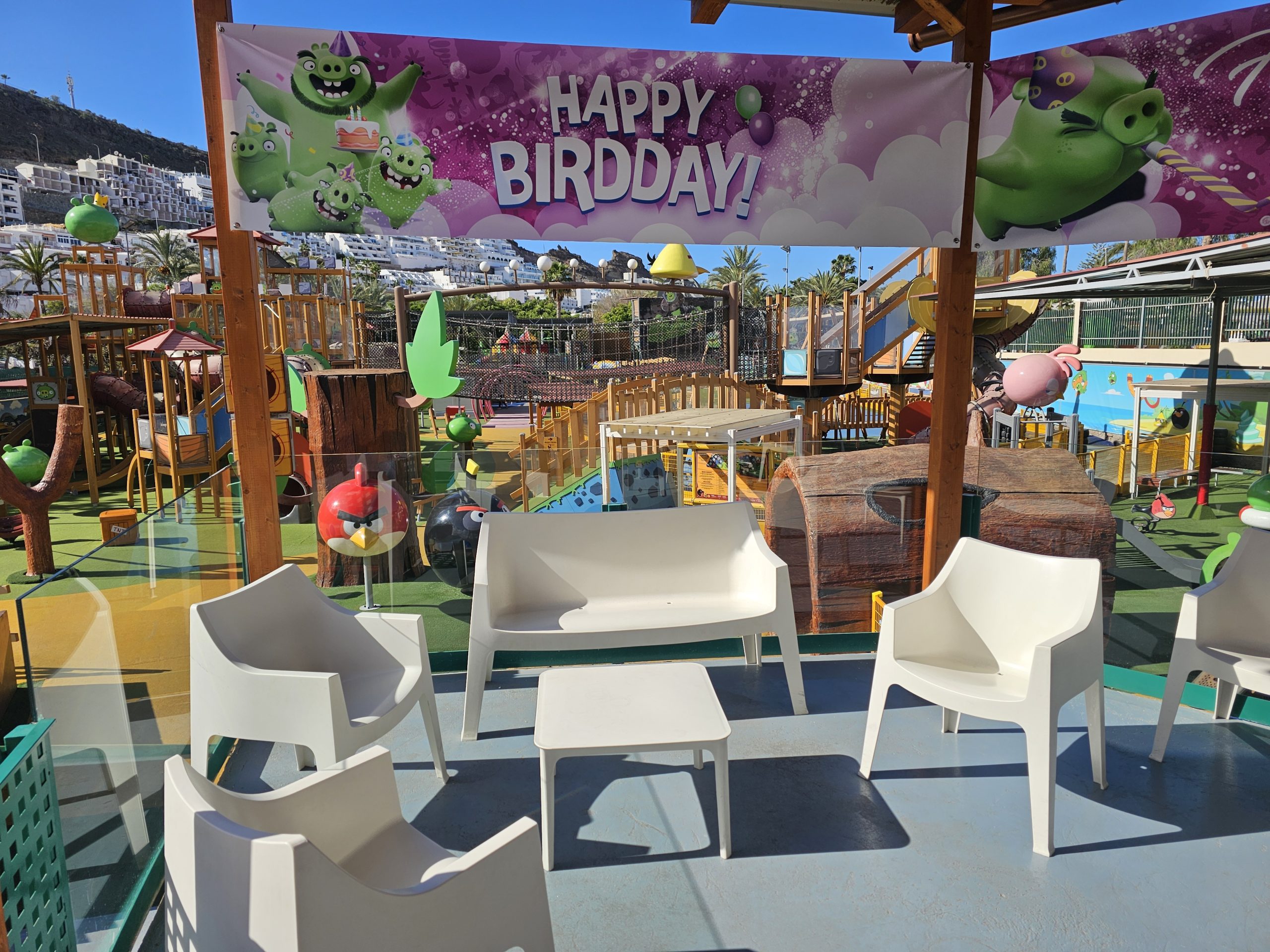 Outdoor play area with seating and 'Happy Birdday' banner with cartoon birds and pigs.