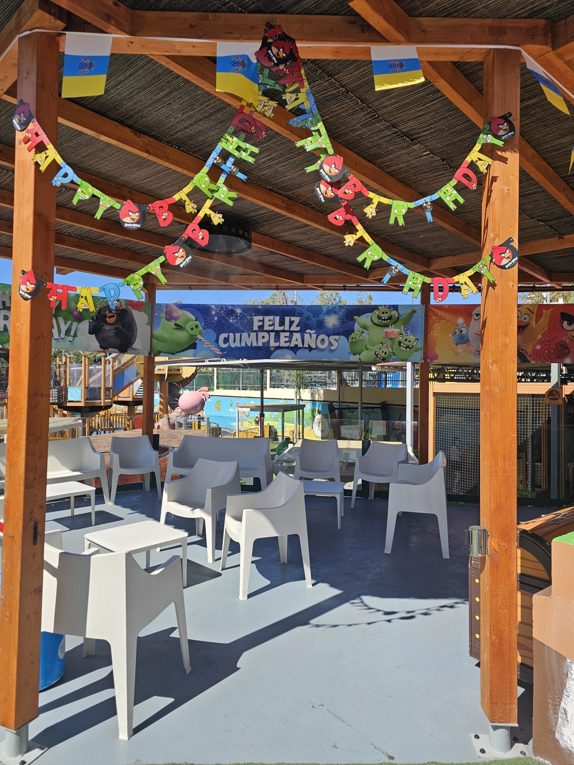 Outdoor birthday setup with colorful banners and chairs under wooden pergola.
