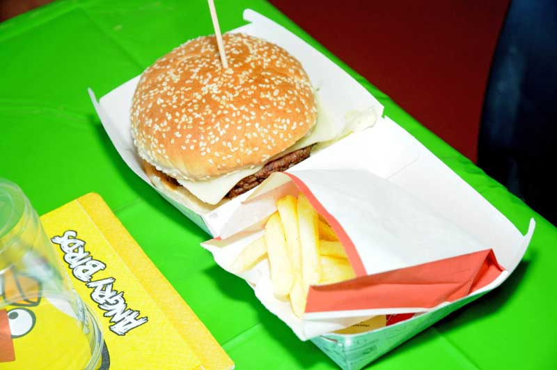 Cheeseburger with fries in a fast-food box on a green table.