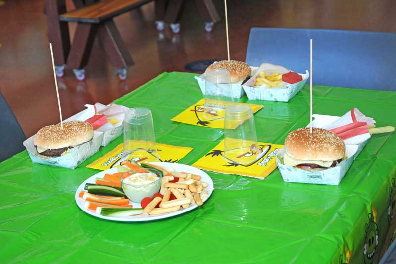 Table with burgers, plates of fries, vegetable platter, and colorful napkins on a green tablecloth.