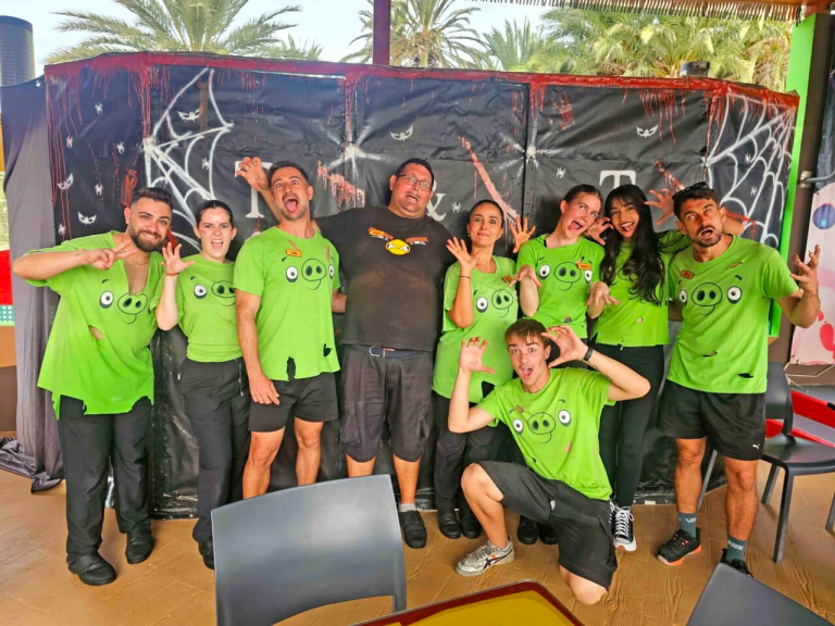 Group in green shirts posing playfully with spider web backdrop.