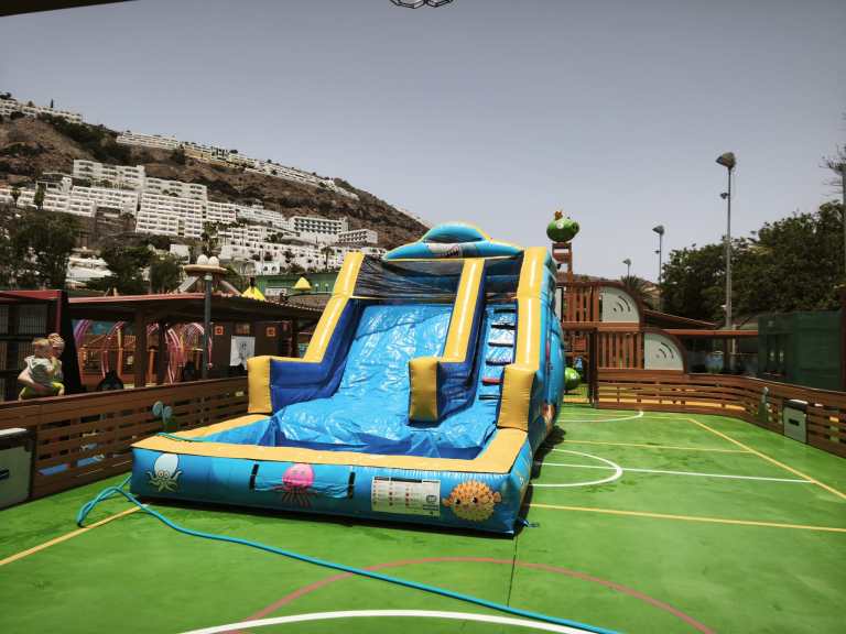 Inflatable water slide on a sports court with mountains in the background.