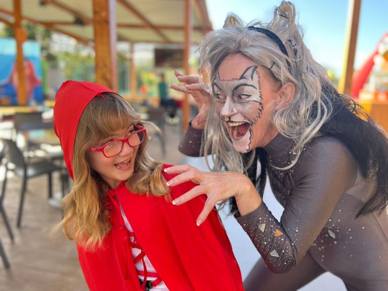 Child in red cape and playful adult in wolf costume outside.