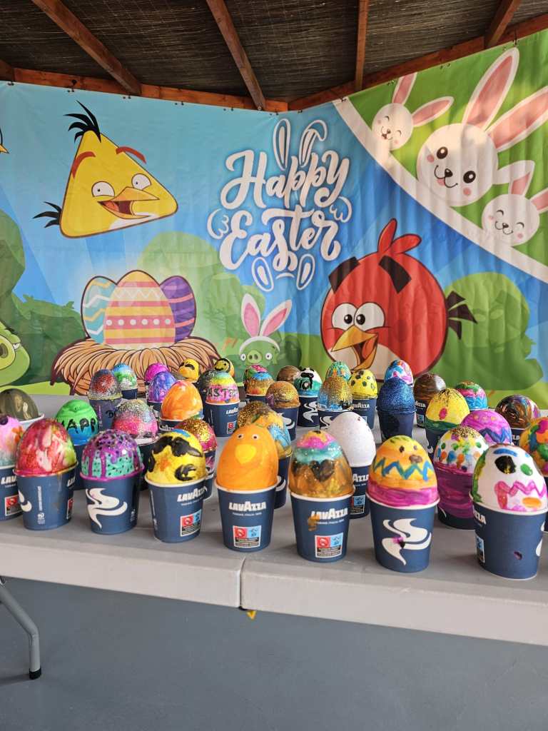 Decorated Easter eggs on cups, Angry Birds backdrop with 'Happy Easter' sign.