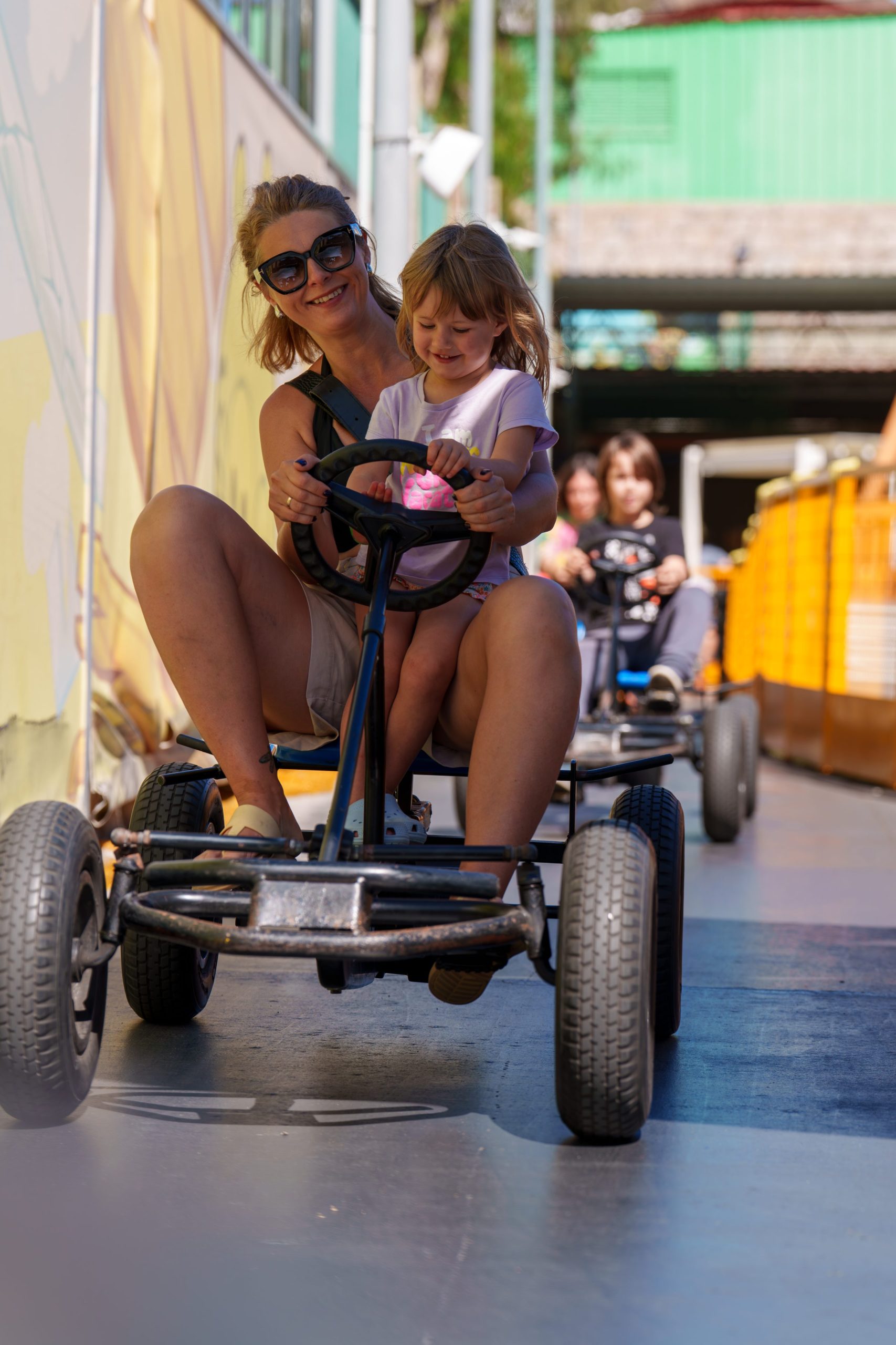 Woman and child happily riding a pedal go-kart at an amusement park.