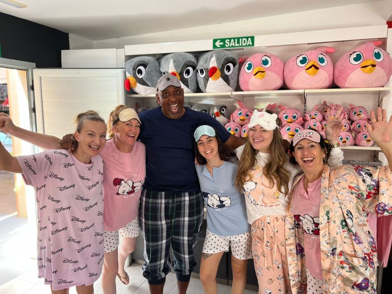 Group of smiling people in pajamas with cartoon print, posing in front of stuffed toys on shelves.