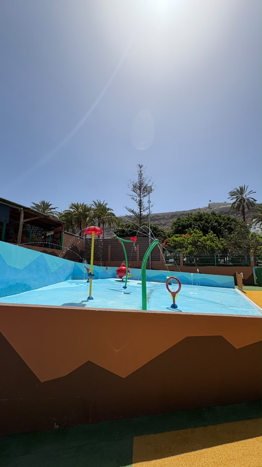 Playground splash pad with water jets under a clear sky.
